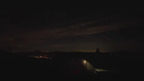 Dark shot of a man stood beside an illuminated tent on a hill at night Vidéo 281792013