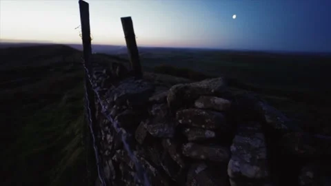 Dark shot of an old stone wall and barbed wire fence at dawn with the moon Stockbeeldmateriaal 130468527