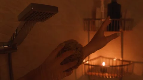 Dark showering woman's hand holding a natural sponge under flowing shower water, Stock Footage 338128155