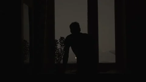 Dark silhouette of man approaches window and looks out into night snow storm. Stock Footage 221967064