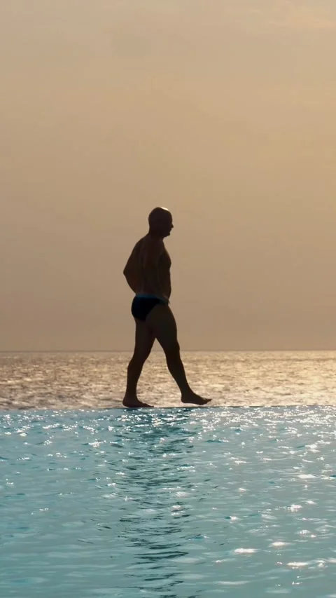 Dark silhouette, man walking on edge of outdoor infinity pool with panoramic sea Stock Footage 315216184