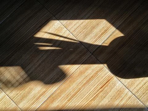 Dark silhouette shadows falling on brown wood grain ceramic floor tiles Stock Photos