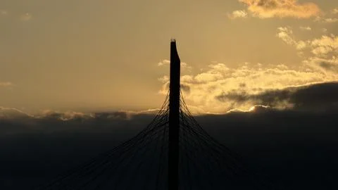 Dark silhouette of a tall cable-stayed bridge pylon against a vibrant golden Stock Photos