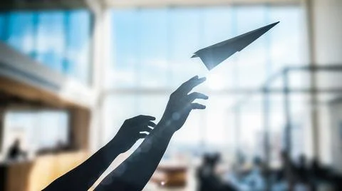 Dark silhouetted human hands energetically launch folded paper airplane upwar Stock Photos
