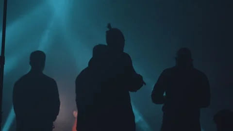 Dark silhouettes of men from the back in a dark hangar lit by blue rays. Stock Footage 160970321