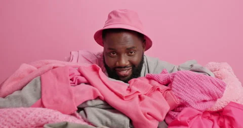 Dark skinned bearded guy raised head covered with pile of unfolded laundry Stock Footage 156633431