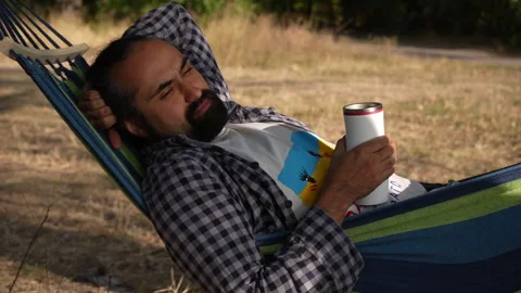 A dark-skinned bearded man is relaxing in a hammock with squinted eyes. Stock Footage 252485844