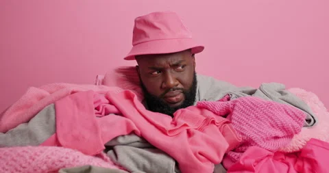 Dark skinned bearded man sticks head from pile of dirty clothes prepares for 库存影片 156225658