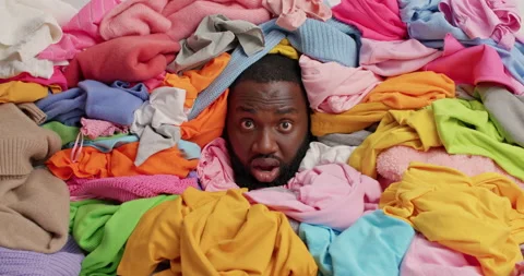 Dark skinned bearded man sticks head through pile of multicolored laundry has Stock Footage 156226723