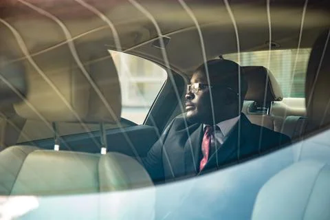 A dark-skinned businessman in a suit in the back seat of a luxury car looks out Stock Photos