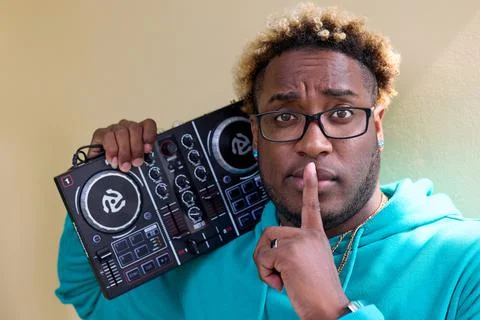 Dark skinned guy with serious expression holds DJ remote on his shoulder Stock Photos