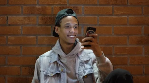 Dark skinned guy sitting on the floor and chatting on his phone and smilling Stock Footage 115915484