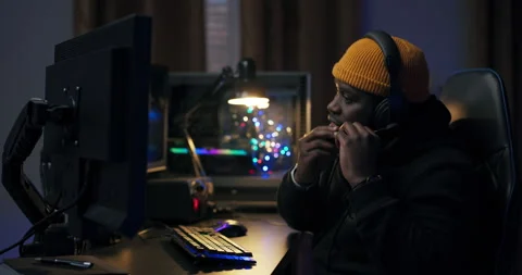 Dark-skinned guy in a yellow cap sits at desk getting ready to play a video game Stock Footage 178741617