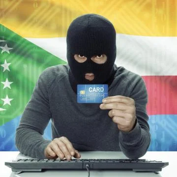 Dark-skinned hacker with flag on background holding credit card - Comoros Stock Photos