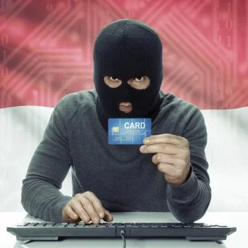 Dark-skinned hacker with flag on background holding credit card - Indonesia 스톡 사진