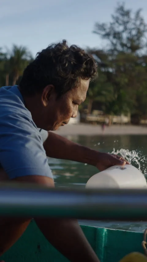 Dark-skinned man bailing water from his boat on the beach Stock Footage 265470407