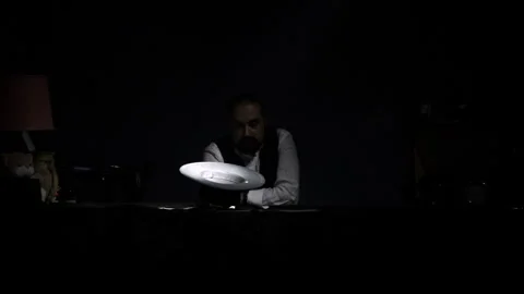 A dark-skinned man with a beard in a shirt and vest sits at a table and holds Stock-Footage 241495154