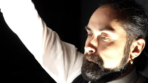 A dark-skinned man with a beard in a shirt and vest draws with a brush intently Stock Footage 242163378
