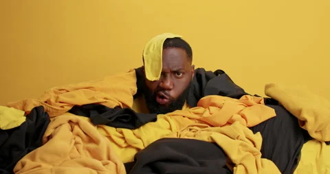 Dark skinned man collects laundry for washing poses near pile of clothes has Stock Footage 156228544