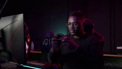 A dark-skinned man with glasses plays a game in the app on his smartphone and is Stock Footage 151497205