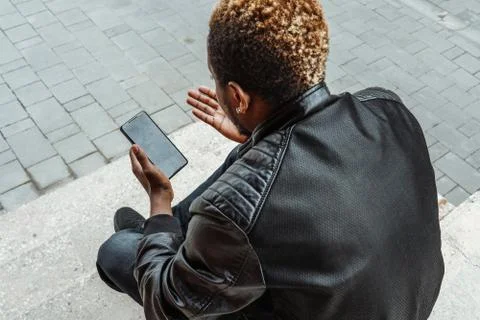Dark-skinned man looking at mobile phone screen and sitting on concrete steps. Stock Photos
