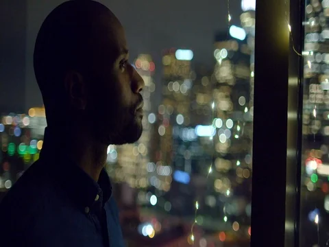 Dark skinned man sips drink at window overlooking nighttime LA 4K Stock Footage 73103164