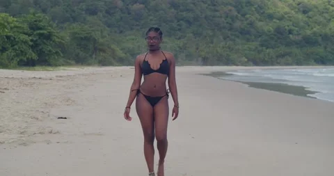 A dark-skinned model in a black bikini posing in the midday sun on a pristine Stock Footage 335120945