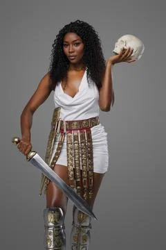 Dark-skinned model in white tunic an ornate belt holds gladius sword and skull 库存照片