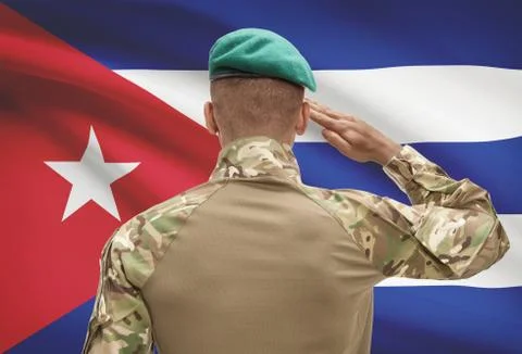 Dark-skinned soldier in hat facing national flag series - Cuba Stock Photos
