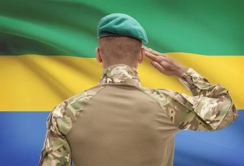 Dark-skinned soldier in hat facing national flag series - Gabon 스톡 사진