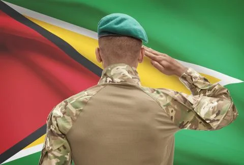 Dark-skinned soldier in hat facing national flag series - Guyana Stock Photos