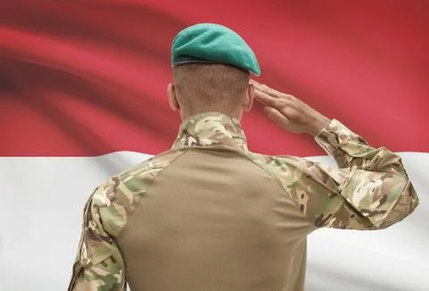 Dark-skinned soldier in hat facing national flag series - Monaco Фото