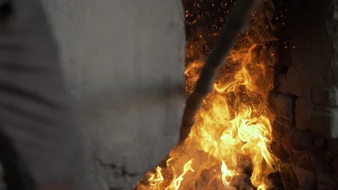A dark skinned worker poking and adjusting a fire with a wooden stick. Stock Footage 144660711