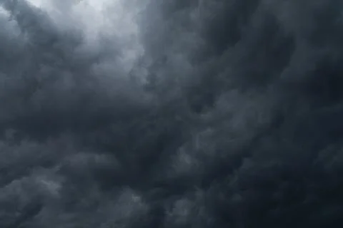 A dark sky filled with clouds and a small bright spot. Stock Photos