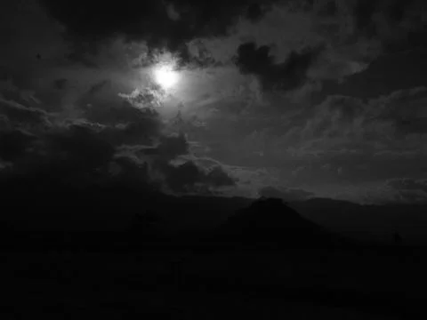 A dark sky with a full moon and a mountain in the background Stock Photos