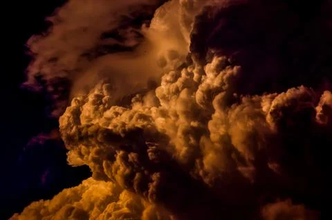 A dark sky with a large cloud that is orange and brown 写真素材