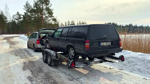 Dark station wagon loaded on a car trailer behind another vehicle on a snowy Stock Footage 333326091