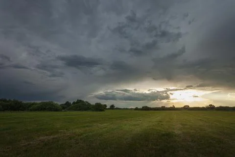 Dark storm cloud and sunlight over the meadow Stock Photos