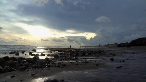 A dark storm cloud creeps into the sunset at a rocky beach Stock Footage 74290199
