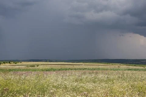 A dark storm cloud hangs far over the valley and heavy rain is falling Stock Photos
