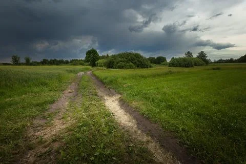Dark storm cloud over meadow with dirt road 库存照片