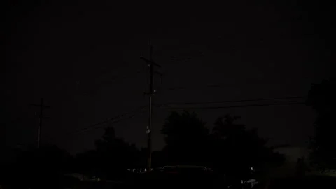 Dark storm clouds and lightning illuminating the night sky above power lines Stockbeeldmateriaal 346790437
