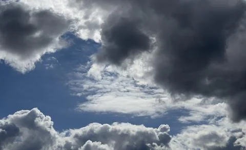 Dark storm clouds frame a blue sky. Bright cloud edges contrast with open spa Stock Photos