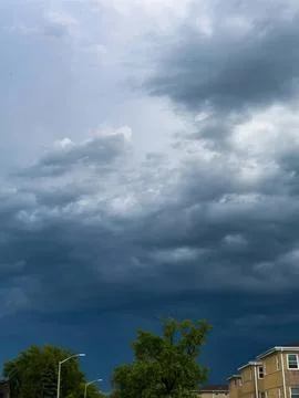 Dark storm clouds gather in a cloudy sky over houses Stock Photos