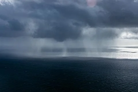 Dark storm clouds gather over the ocean, with rain falling in the distance,.. Fotos Stock