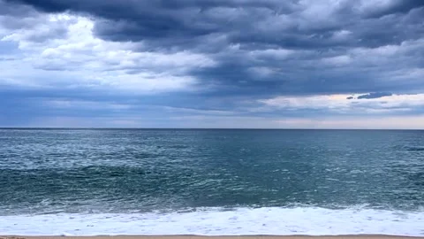 Dark storm clouds gathering over sea as waves roll toward sandy beach. Dramatic Stock Footage 343624138