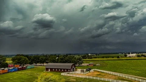 Dark Storm Clouds Gathering Over a Rural Farmhouse With Fields and a Fence .. Stock Photos