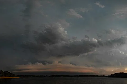 Dark storm clouds gathering over the lake during a dramatic sunset Stock Photos
