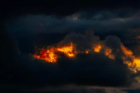 Dark storm clouds illuminated by vibrant orange and yellow hues at sunset, .. Stock Photos
