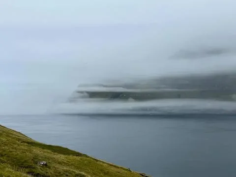 Dark storm clouds over a calm lake with green hill Stock Photos